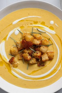 A creamy cauliflower curry soup topped with crunchy croutons and rosemary, styled on a white