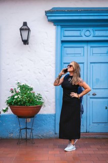 A full shot of a woman wearing a black dress and sunglasses, talking on the phone while looking up.