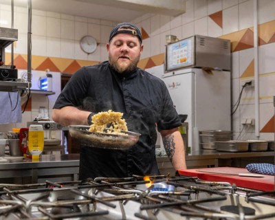 A chef in a black uniform expertly prepares a dish in a professional kitchen, showcasing skill and