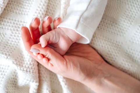 A tender moment as a mother gently holds her newborn baby's tiny hand. The warm scene speaks of