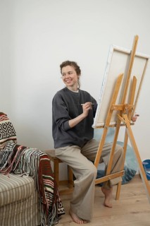 Smiling artist enjoying painting at an easel in a cozy home studio. The scene captures the