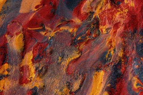Close-up of an abstract, swirling texture combining metallic paints in vivid shades of red, gold,