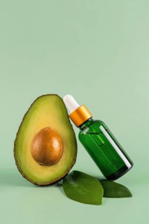 Minimalist image of a green dropper bottle alongside a half avocado on a soft green background.
