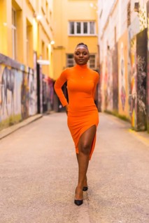 Fashionable urban style with a black African girl in an orange dress and black heels on a city
