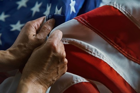 A close-up image showcases hands gently grasping the fabric of an American flag, emphasizing the