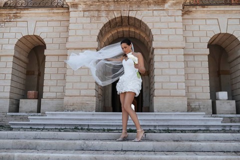 A bride in a white dress gracefully descends stone steps at an ancient villa in Treia, Macerata,