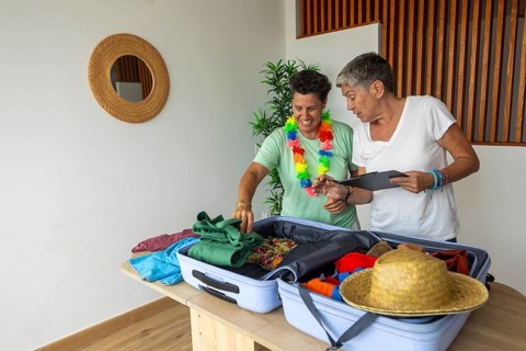 Two mature lesbians joyfully preparing their luggage for a summer holiday, choosing clothes and