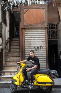 Cairo, Egypt. April 15th 2025. A young Egyptian man sits on a bright yellow motor scooter, a