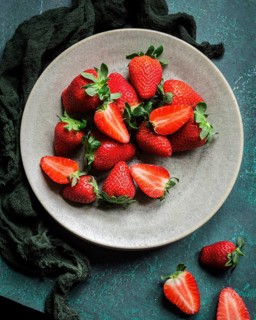 A ceramic plate filled with vibrant red strawberries, some cut in half, placed on a textured green