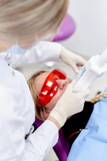 A dentist in a dental clinic uses a laser device for teeth whitening. The patient is wearing