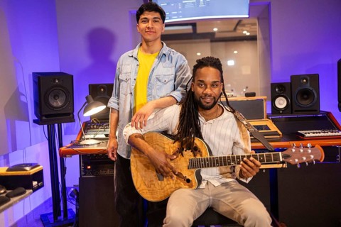 Two musicians in a professional recording studio, surrounded by sound equipment and instruments.