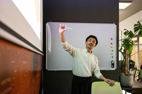 A professional giving a presentation in a modern office. The projector screen, whiteboard, and a
