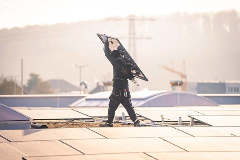 Worker lifts solar panel on a sunny roof for installation, PV assembly at OBI Baumarkt, Mühlacker,