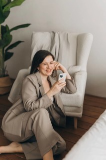 A young professional in a beige suit relaxes on a cozy, textured armchair, using a smartphone. The