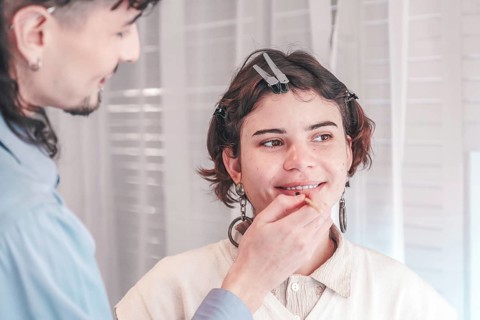 Professional makeup artist applying lip liner on a smiling model in a bright, modern beauty salon,