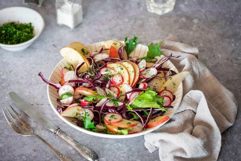 A vibrant salad featuring red cabbage, radishes, apple slices, and mixed greens. Served on a rustic