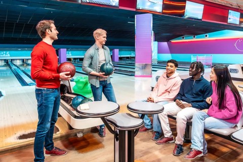 Multi ethnic group of young friends having fun and playing bowling together at the bowling alley