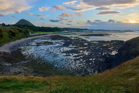 Coastal landscape at sunset with beach, rocks and hills in the background, North Berwick, East