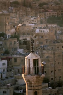 A mosque minaret with dawn sunlight set against a backdrop of traditional hillside houses in the