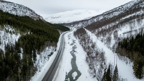 A breathtaking aerial view captures a Nordic winter landscape, showcasing a road alongside a