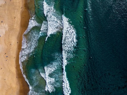 Aerial view of ocean waves meeting a sandy beach of Sydney. The turquoise sea contrasts with the