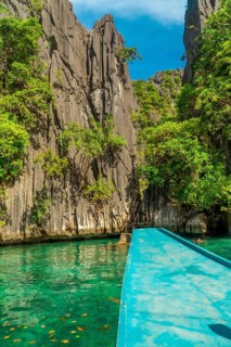 Traditional turquoise boat sailing on calm water between huge limestone cliffs in paradise twin