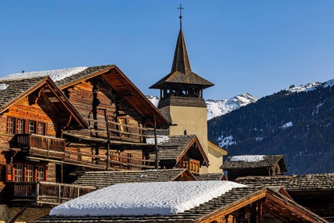 Snow-covered roofs of old farmhouses and barn storage, in the back the church tower of the Saint