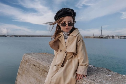 Young girl in a trench coat and beret poses stylishly by the sea in Civitanova, Italy. Her