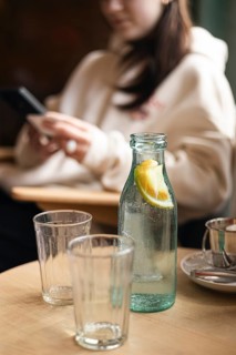 Cropped unrecognizable blurred young woman in a cafe, engaged with her smartphone near a cold water