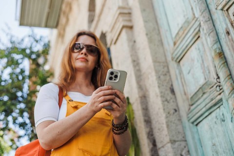 From below a woman in her 40s, dressed in orange and yellow, uses her smartphone as she explores