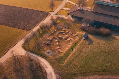 Curvy area of earth seen from above near a building, with surrounding fields and country road, bike