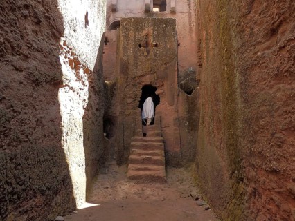 A person dressed in white enters a rock church through a narrow alley, UNESCO World Heritage Site,