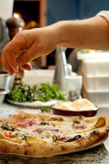 Cropped unrecognizable person sprinkling cheese over a freshly baked pizza in a home kitchen, with