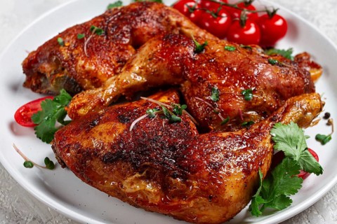Grilled fried chicken legs, served, with fresh cherry tomatoes, and herbs, on a white plate,