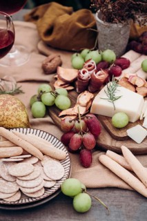 A rustic charcuterie board featuring an assortment of snacks including grapes, cheese, cured meats,