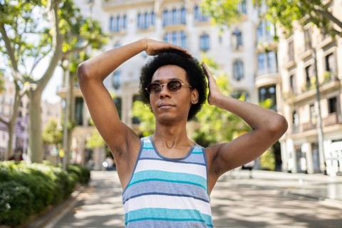 A confident non-binary person wearing sunglasses poses outdoors, enjoying a sunny day in the city.