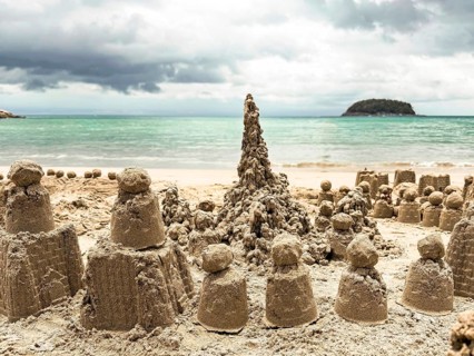 A collection of intricately crafted sand castles adorns the sunlit seashore. The ocean's gentle