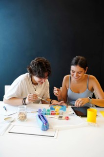 Two cheerful teenagers, a non-binary individual and a female, engage in a creative painting