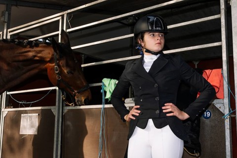 A dressage competitor in formal attire poses confidently next to a stabled horse The scene