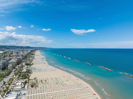 Drone photo showing a long stretch of sandy beach lined with umbrellas and a coastal town in