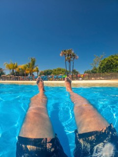 Legs of a tourist floating and relaxing in a swimming pool at a water park during summer vacation