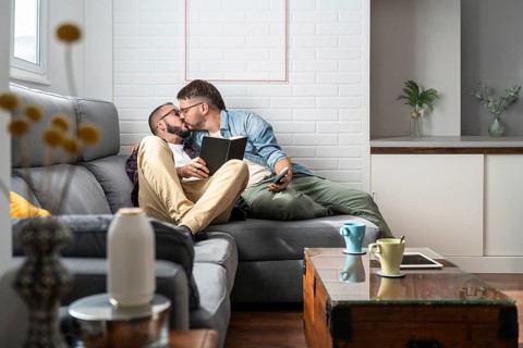 A loving gay couple shares an intimate moment kissing on a comfortable sofa in a modern living