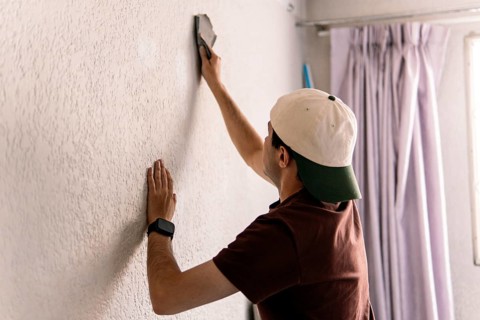 Unrecognizable man from behind plastering a white wall as part of a home remodeling project,