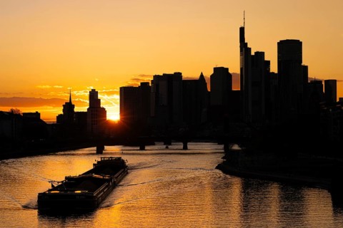 The sun sets behind the skyscrapers of Frankfurt's banking skyline as a barge sails along the Main,