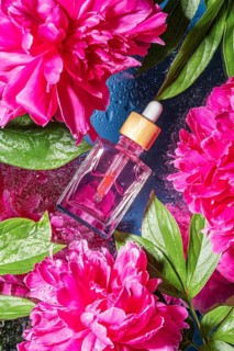 Top view of a pink serum in a glass dropper bottle on a textured blue background, surrounded by