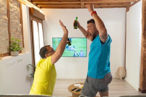 Excited friends celebrating a goal with raised arms while watching a live sports match on