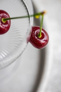 From above, a ripe cherry sits inside a textured glass, showcasing its vibrant red color and fresh