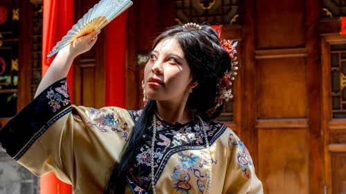 A young woman dressed in traditional Qing Dynasty attire poses with a fan in Pingyao, China. Her