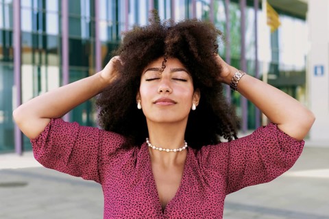 Young Arab woman with afro hair, eyes closed, enjoying a sunny day. She is wearing a patterned