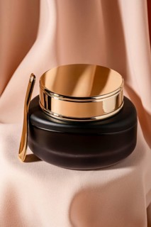 A luxurious black cosmetic jar with a gold lid and spatula on soft, flowing beige curtain The